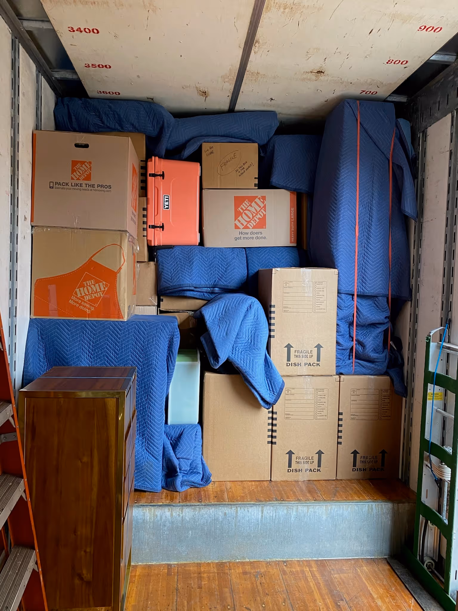 Packed moving truck with boxes, a Yeti cooler, and furniture wrapped in blue blankets.