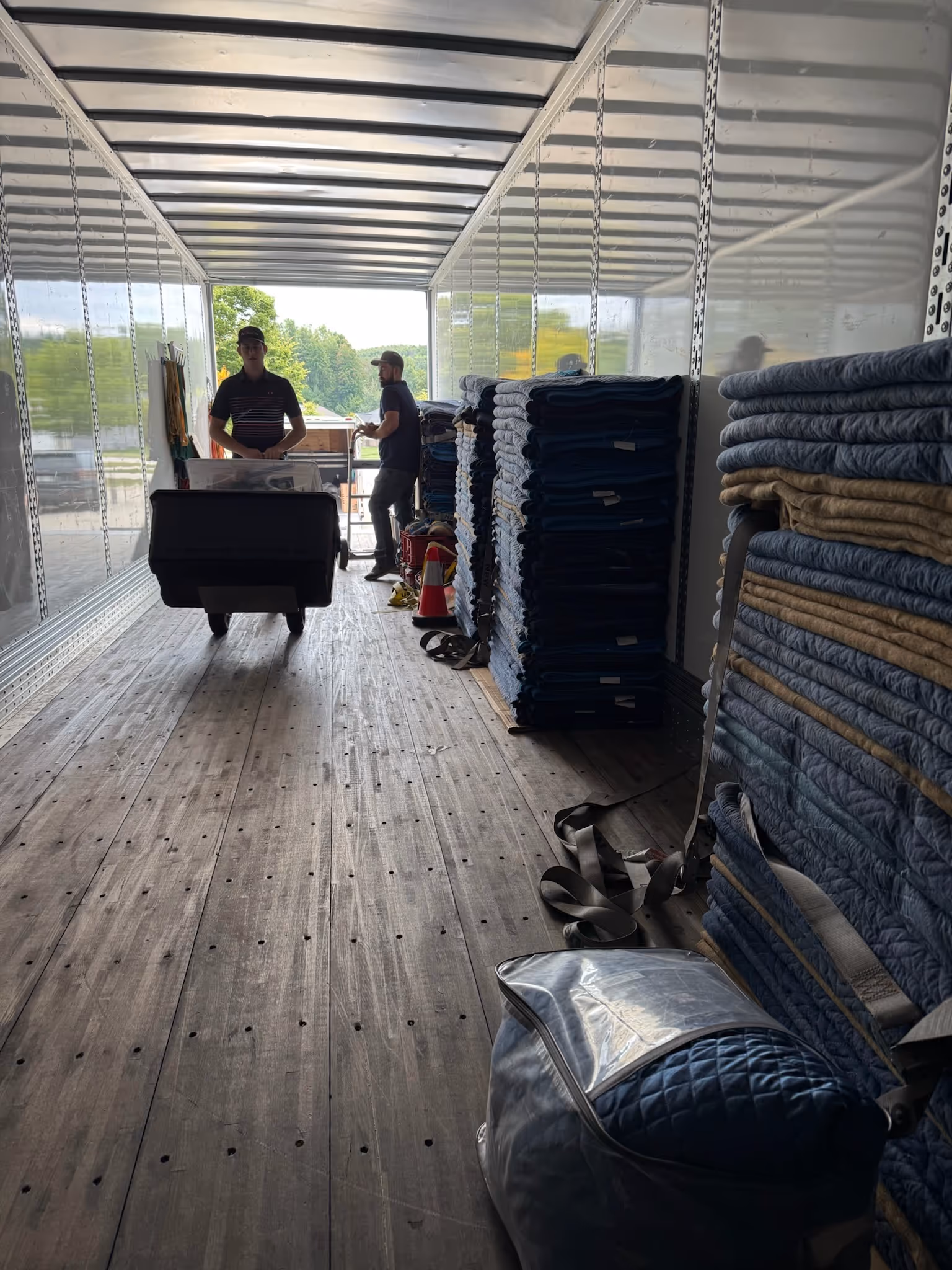 Two men inside a truck unloading stacked moving blankets and equipment.
