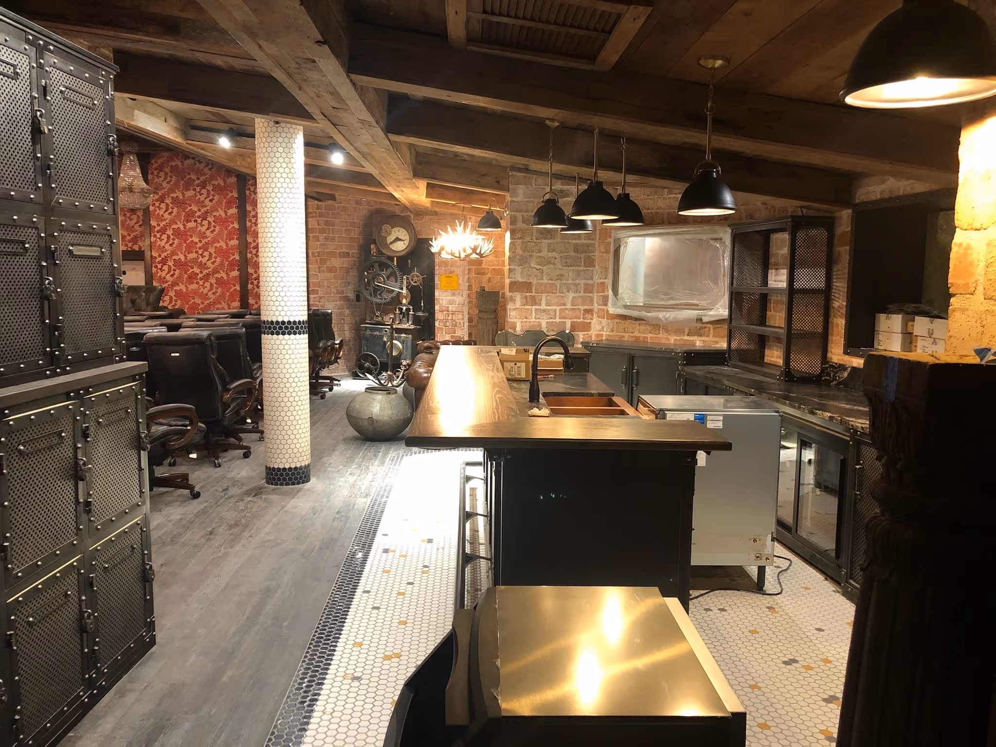 Industrial-style basement room with a bar, pendant lights, office chairs, and exposed brick walls.